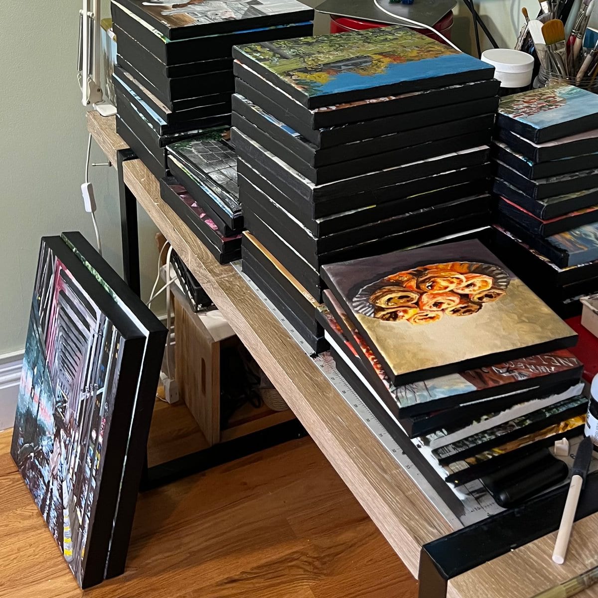 Stacks of finished canvases and framed artwork piled on a table